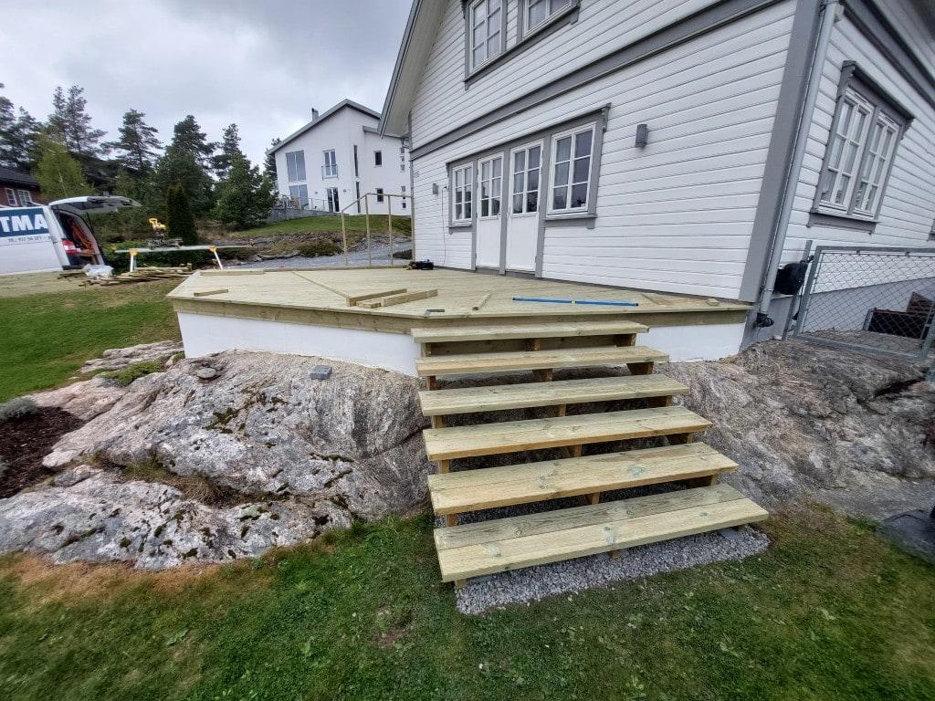 Ny terrasse med trapp i impregnert tre, bygget over svaberget foran et hvitt hus