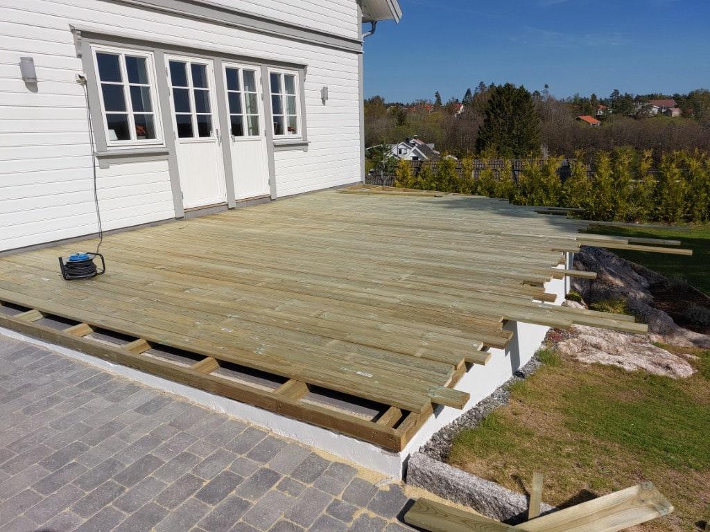 Ny terrasse i impregnert tre foran et hvitt hus